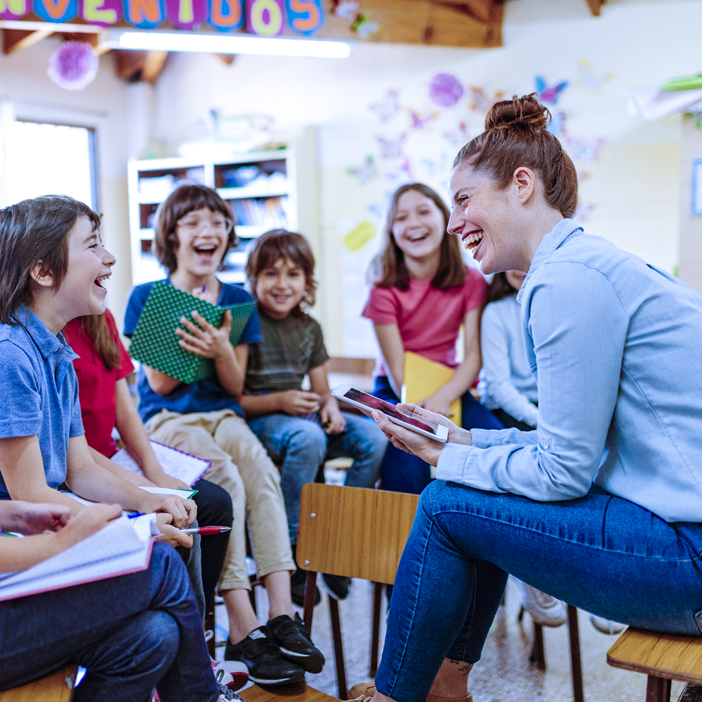 Profissional de educação em sala de aula com 5 alunos, meninos e meninas, representando o cuidado humanizado e a atenção integral oferecida por sistemas de gestão em educação pública.